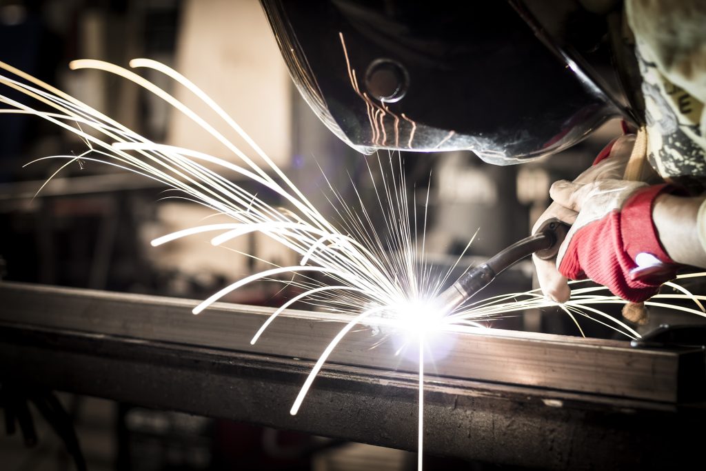 A person welding a metal object, creating bright sparks that illuminate the workspace around them.